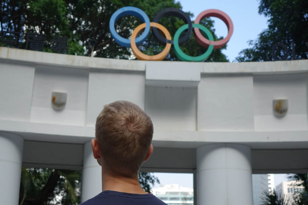 Die 5 Olympia Ringe auf dem Olympia Monument in Hong Kong ueber dem Kopf von Henning Roxin